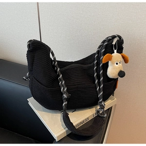 Detail of black corduroy crescent bag featuring a textured strap and plush Gromit pendant