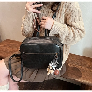Retro black leather shoulder bag detail with cute bear and basketball charms on a model