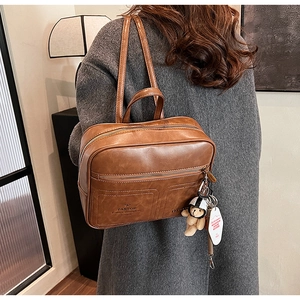 Brown leather backpack with side view showing front pockets and cute bear charm detail