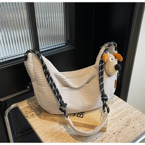 Close-up of beige corduroy dumpling bag with braided rope strap and plush dog charm