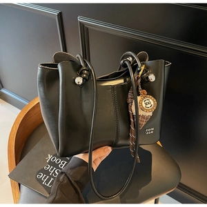Detail of black faux leather tote bag featuring knot handle, silver bead, and plaid scarf