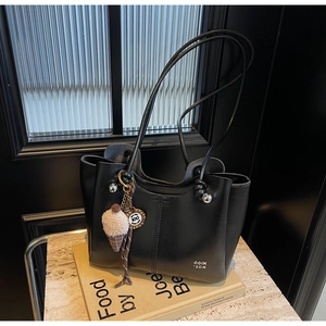 Detail of black leather tote bag featuring fine stitching and ice cream charm accessory