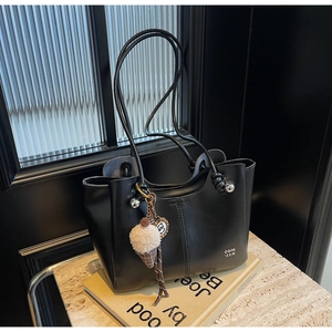 Detail of minimalist black tote bag featuring fine stitching and plush ice cream pendant