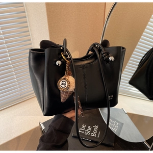 Detail of black tote bag with knotted handles, silver hardware, and plush charm accessory