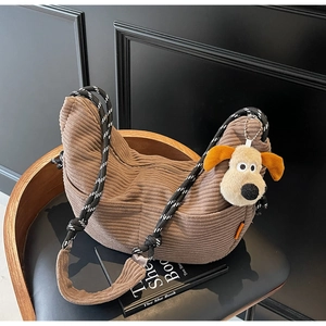 Detail of brown corduroy hobo bag with woven strap and plush dog pendant on a black chair