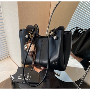 Detail of a black leather tote bag with ball rivet handles and a cute charm accessory