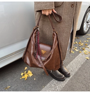 Detail of dark brown tote bag with metal clasp and woven cord on an autumn coat