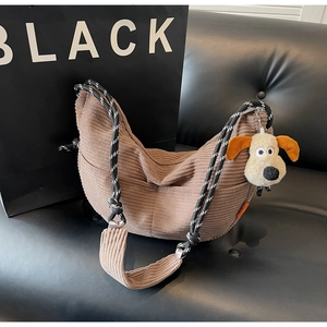 Close-up of brown corduroy crescent bag featuring woven rope strap and plush dog charm