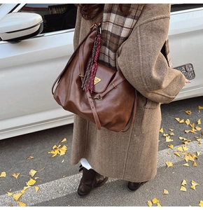 Close-up of vintage brown tote bag with metal logo and woven strap detail in autumn street