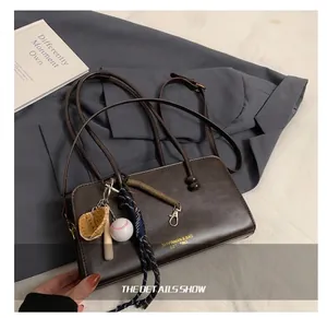 Detalle del bolso Boston de cuero marrón oscuro con dijes de béisbol y bate