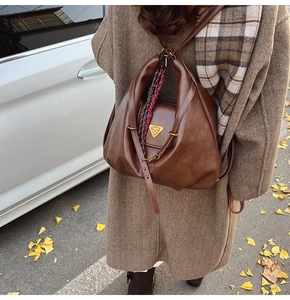 Close-up of vintage brown leather backpack with golden metal logo and silk scarf detail