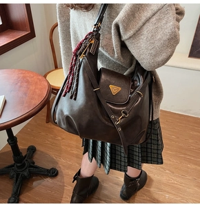 Detailed view of brown leather Hobo bag with metal logo and woven tassel accessory