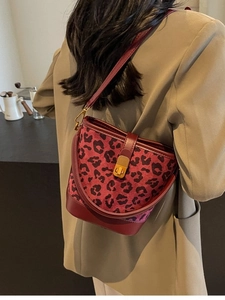 Burgunderfarbene Bucket Bag mit Leopardenmuster und Goldbeschlägen an einem Model im Café