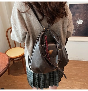 Detail of dark brown leather backpack with golden triangle hardware and woven charm accessory