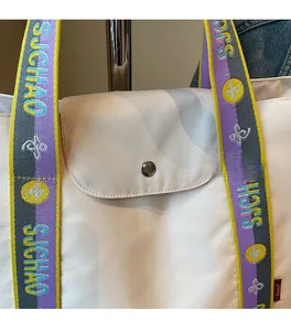 Detail of white nylon tote bag with colorful woven strap and silver snap closure button