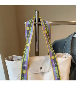 Detail of cream tote bag featuring a wide woven colorful shoulder strap with SJCHAO text