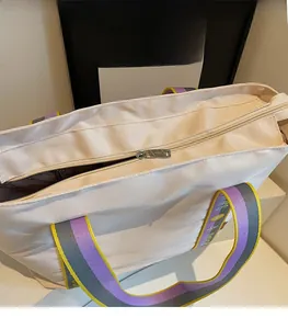 Detail of smooth metal zipper and colorful woven strap on a beige canvas tote bag