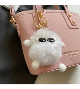 Close-up of white plush monster keychain charm with sunglasses and golden metal chain