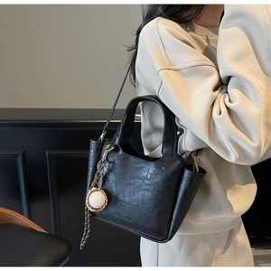 Détail du sac seau vintage noir avec texture cuir et accessoire de charme de baseball