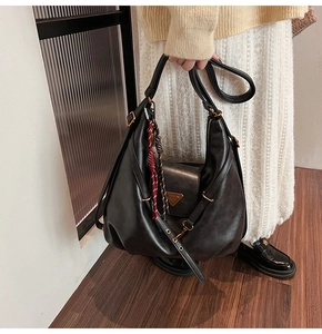 Detail of black matte leather hobo bag with vintage gold logo and woven silk scarf