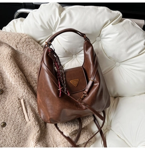 Detail of a brown leather hobo bag with a gold triangle logo on a cozy white fleece