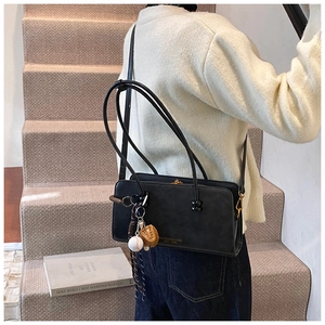 Detalle de bolso de hombro en cuero sintético negro con colgante de béisbol y logotipo