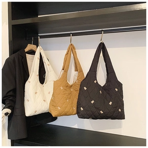 Detailed shot of quilted tote bags in white, tan, and black with small gold bear embroidery