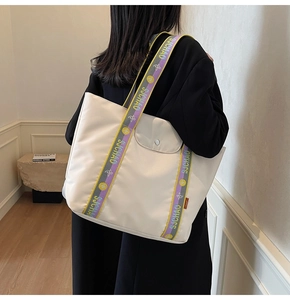 Detail of cream tote bag featuring a multi-color woven strap with floral patterns