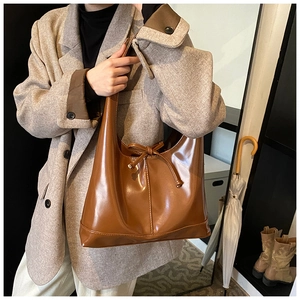 Macro detail of the brown tote bag featuring a decorative bow tie and retro leather texture