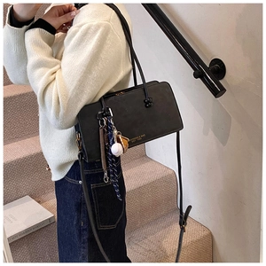 Detalle del bolso de hombro en cuero negro con colgantes de béisbol y logotipo dorado