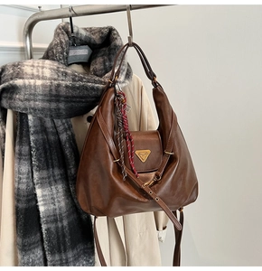Detail view of a large brown vintage tote bag with a golden metal triangle plaque