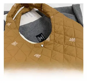 Detail of brown quilted tote bag featuring bear embroidery and silver snap button closure