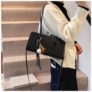 Detalle del bolso de hombro negro con colgante de béisbol y borla de rayas decorativa