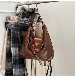 Detail of vintage brown leather hobo bag with gold triangular plaque and woven pendant
