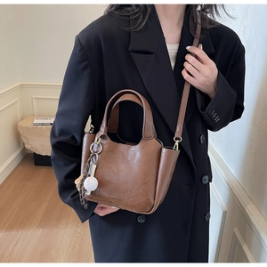 Détail d'un sac seau en cuir marron foncé à texture litchi avec pendentif de baseball