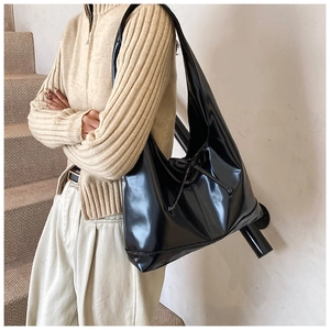 Detail of a large black patent leather hobo shoulder bag with drawstring detail