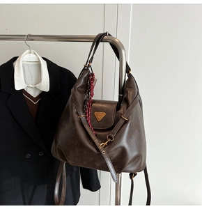 Detail of retro dark brown leather tote with gold metal logo and decorative silk scarf