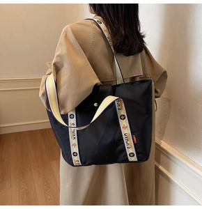 Detail of black nylon tote bag with colorful lettered strap and snap button closure