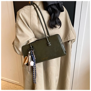 Detalle de bolso verde oscuro en piel sintética con colgante de béisbol y correas