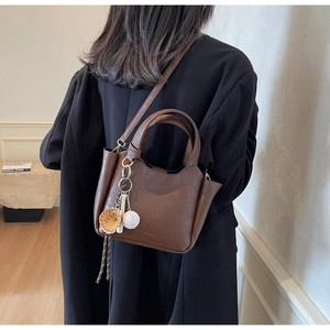 Modèle portant un sac seau en cuir marron foncé avec breloques de baseball