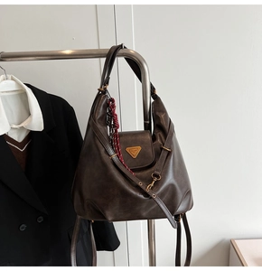 Close-up of retro dark brown leather bag featuring a gold triangle logo and woven pendant