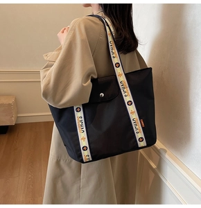 Detail of the black tote bag featuring a bicolor embroidered strap and front pocket