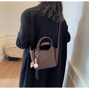 Détail du sac seau en cuir marron foncé avec un pendentif sur le thème du baseball