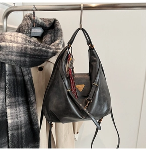 Detail of black matte leather hobo bag with gold triangle logo and woven pendant accent
