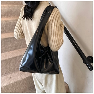 Detail of glossy black leather tote bag featuring side drawstring knot and smooth texture