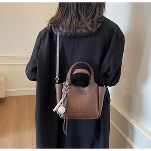 Détails d'un sac seau rétro marron foncé avec pendentif de baseball et texture en cuir