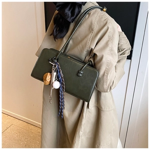 Detalle de bolso de hombro en cuero mate verde oscuro con adornos de béisbol en el hombro