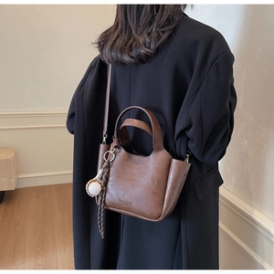 Détail du sac seau vintage marron foncé avec poignées et un charme de baseball