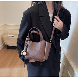 Sac seau vintage en cuir marron porté avec blazer noir et pendentif baseball