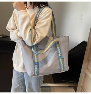 Detail of grey nylon tote bag with blue and yellow woven handles and brand logo